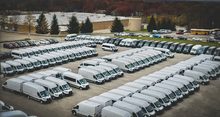 a large fleet storage lot filled with rows of white Mercedes-Benz Sprinter vans and commercial vehicles