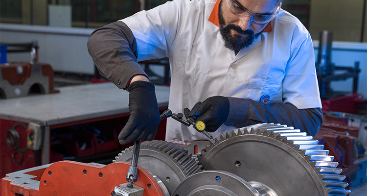 an engineer or technician using a dial indicator gauge to inspect and align industrial gear teeth in a gearbox assembly