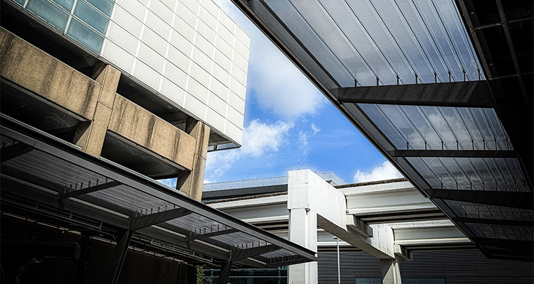 a low-angle, upward view of modern urban infrastructure and buildings framed against a blue sky with scattered white clouds