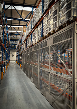 an industrial warehouse interior featuring pallet racking systems equipped with anti-collapse wire mesh safety guards along the lower bays