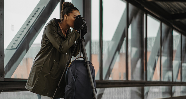 a woman taking a photo with a camera mounted on a tripod inside an architectural structure with large glass windows