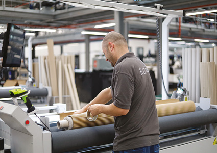 a worker taping a large roll of corrugated cardboard or packaging material on a heavy-duty production machine