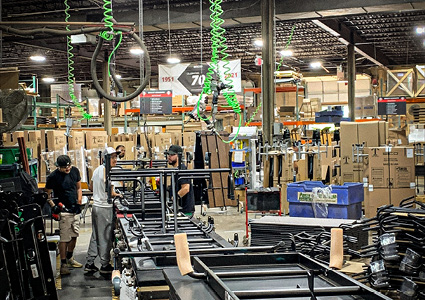 an industrial warehouse or assembly plant floor with workers assembling metal frames