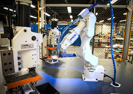 an industrial automated manufacturing cell featuring a white Epson six-axis robotic arm working alongside automated assembly/press machinery